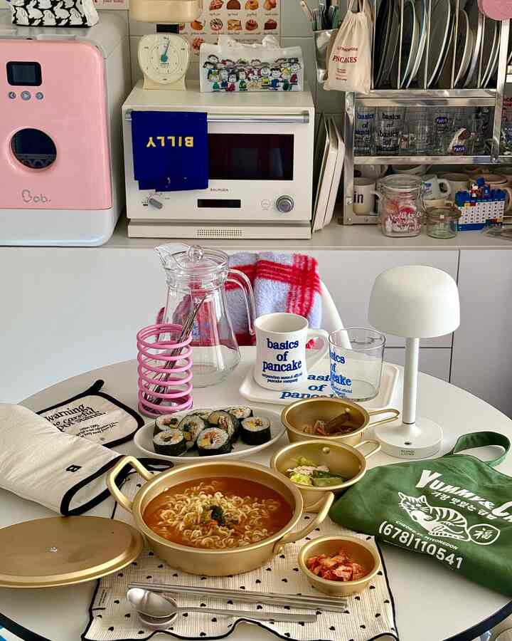 白とゴールドの色調のキッチン、調理器具と料理が並ぶダイニングテーブルが配置されたミニマルで居心地の良い空間