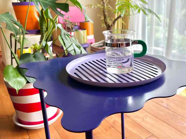 ネイビーブルーのテーブルにガラスと紫のトレイが置かれ、植物とナチュラルカラーが調和するリビングのインテリア