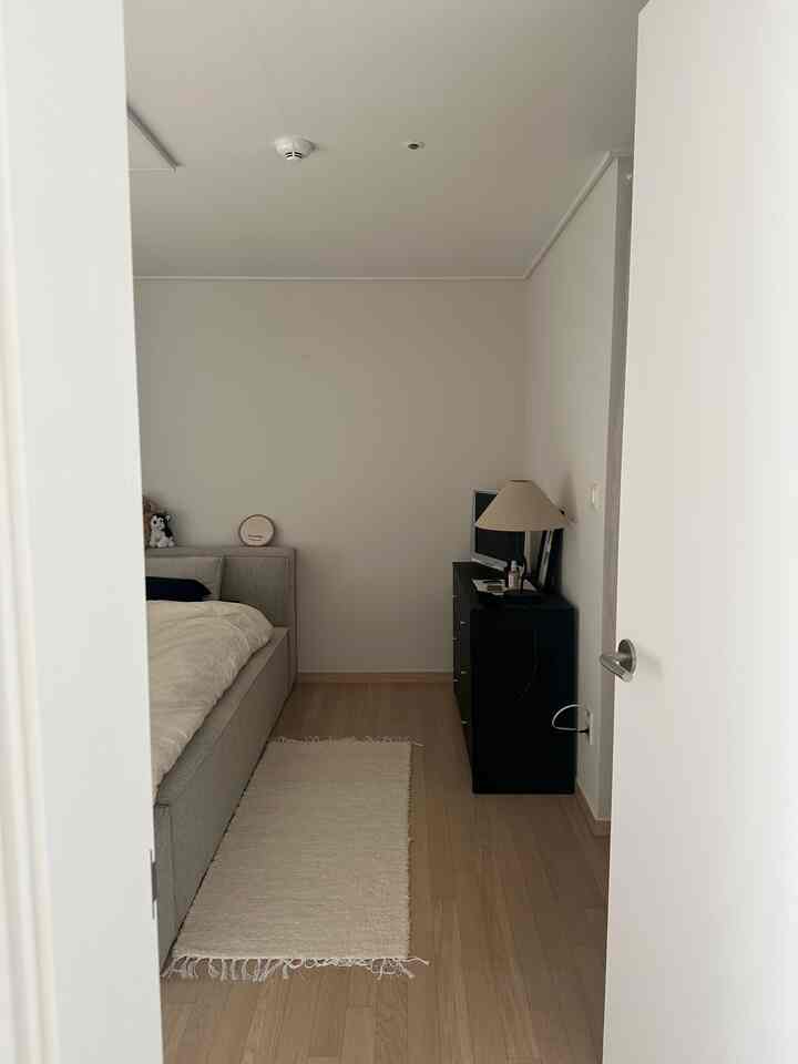 白とベージュの色調の寝室、明るいベッドフレームとラグが温かみのある雰囲気を演出し、黒いチェストがコントラストを成す印象的な空間