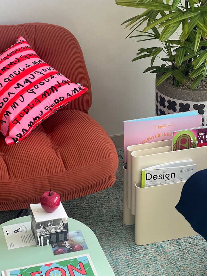 Cozy home office featuring a brown fabric armchair with pink cushion and beige magazine rack with books, set on a blue rug