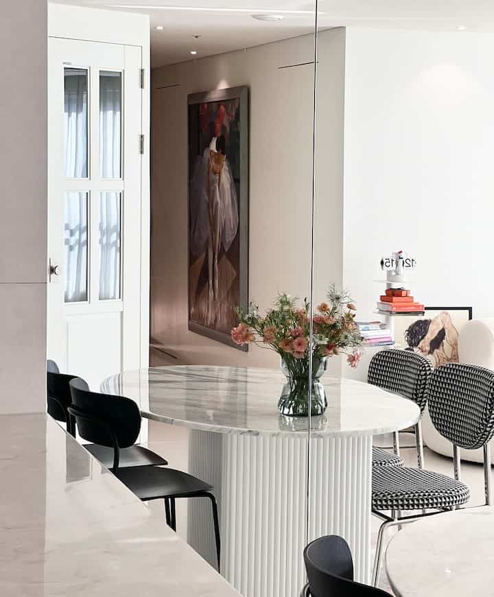 White-toned kitchen featuring a marble round dining table with black and patterned chairs in a modern, neat setting