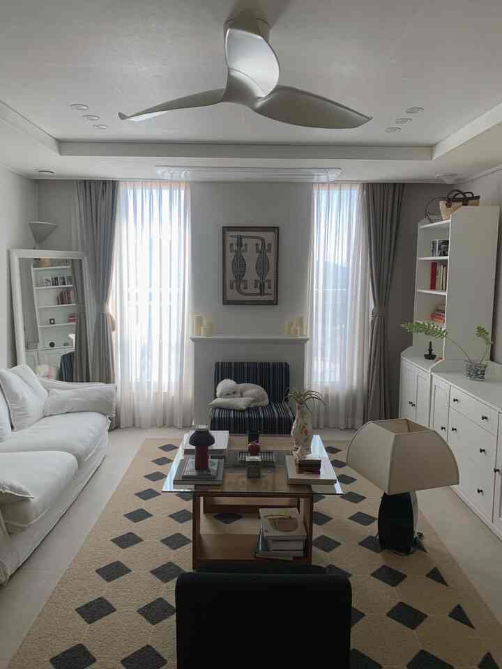 明るい白とグレーのトーンのリビング、一人掛けのストライプソファと白い3人掛けソファ、ベージュのラグの上にガラスの木製テーブルが配置されたモダンな空間