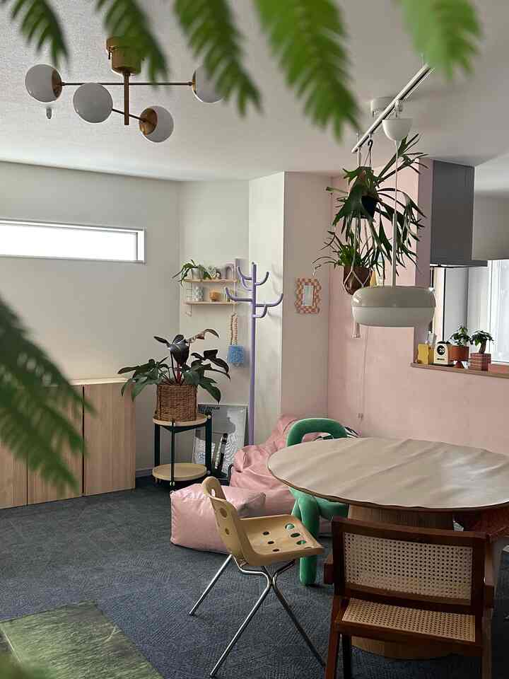 柔らかな自然色と木目調が調和したダイニング、ピンクのビーズクッションとダイニングチェア、吊り植物が配置された雰囲気あるインテリア