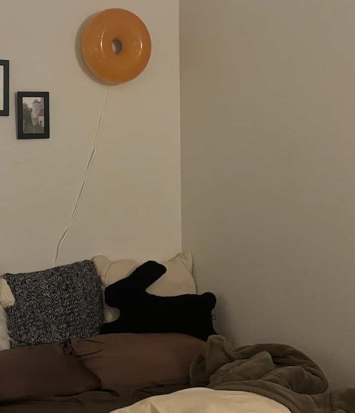 Cozy bedroom in warm brown and black tones featuring a bed with cushions and a distinctive wall-mounted orange light