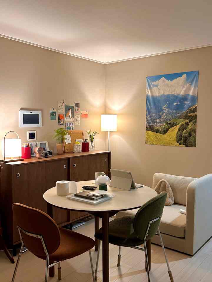 ベージュのトーンのワンルームダイニングスペース、木製収納キャビネットと丸いテーブル、温かみのある照明がある自然な雰囲気のインテリア