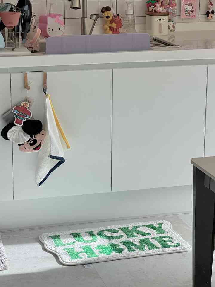 白を基調としたキッチン兼バスルームの明るく清潔感のある空間に、緑のクローバー柄のバスマットが配置されたインテリア