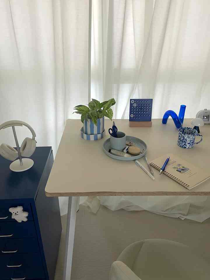 ホワイトとブルーの色調の1DKワークスペース、ブルーの収納キャビネットと植物、机の整理用品が配置された印象的な空間