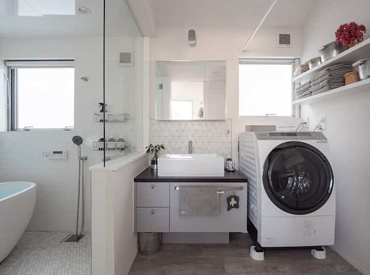 白と自然な色調のモダンなバスルーム、洗面台の鏡と洗濯機、整然としたタオルが配置された雰囲気のあるインテリア