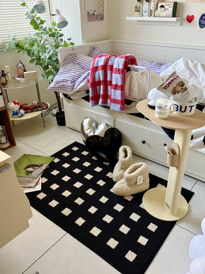 A cozy small bedroom-living room in white and black tones, featuring a checkered rug, heart-shaped cushions, and a green plant