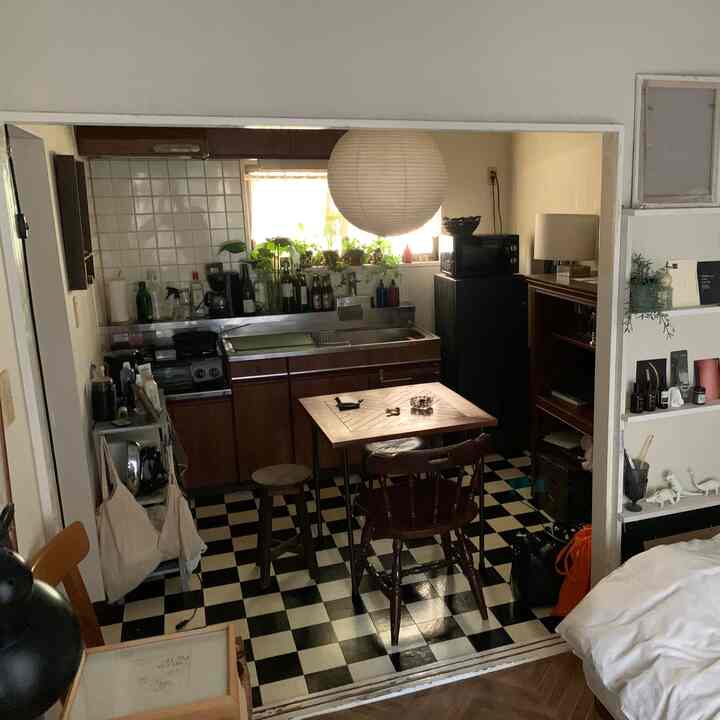 White and brown toned studio apartment kitchen featuring wooden dining table and chairs with a checkered floor, creating a cozy atmosphere