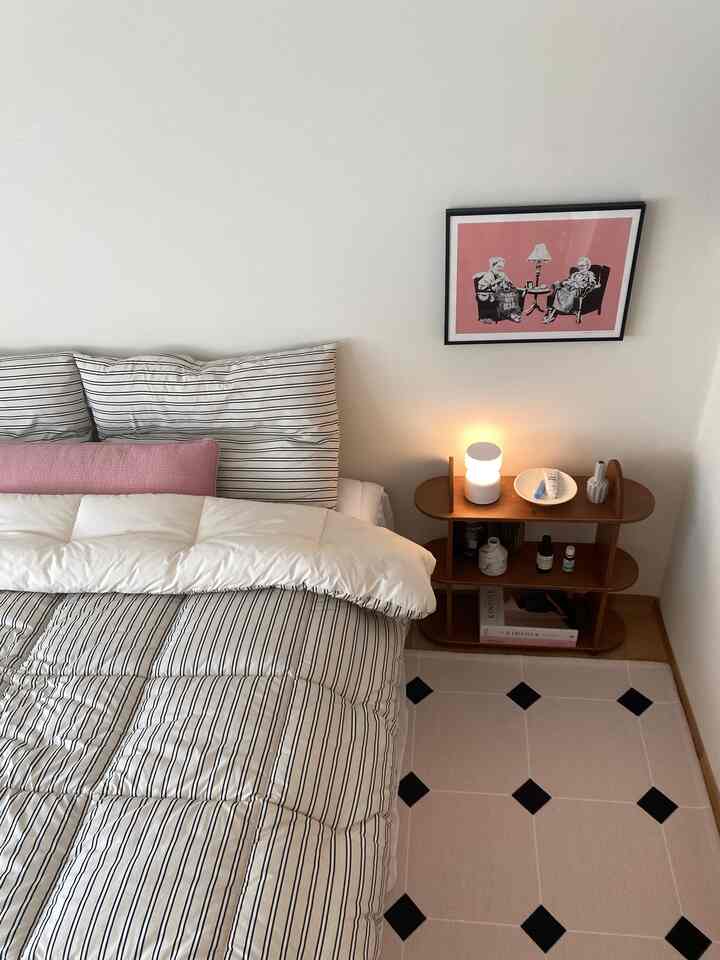 White and natural brown toned bedroom featuring striped bedspread and wooden nightstand in a tidy setting