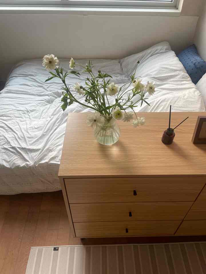 ナチュラルな色調の寝室、白い掛け布団カバーと木製の収納家具が配置された落ち着いた空間