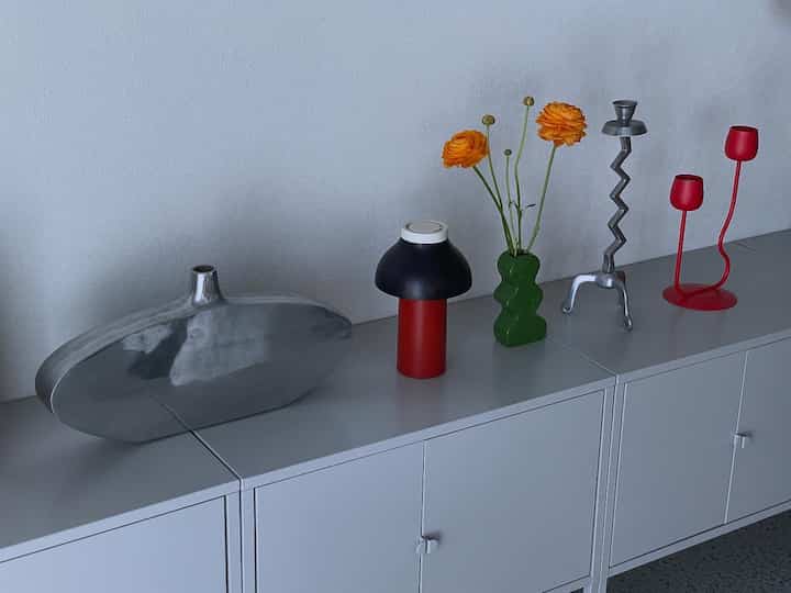 シルバーと赤のトーンの横長の空間、ポストモダンなシルバーのオブジェと独特な花瓶が配置された印象的なインテリア