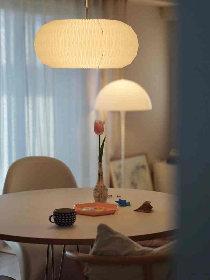 暖かいホワイトトーンのダイニング、丸テーブルにピンクのチューリップ花瓶とオレンジのトレイが置かれたモダンな空間