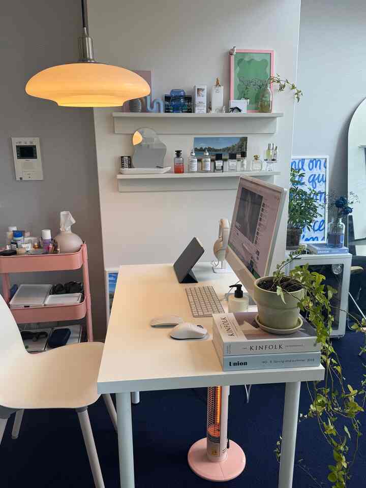 White-toned studio apartment home office featuring a white desk, pendant light, blue carpet, and plants creating a cozy workspace