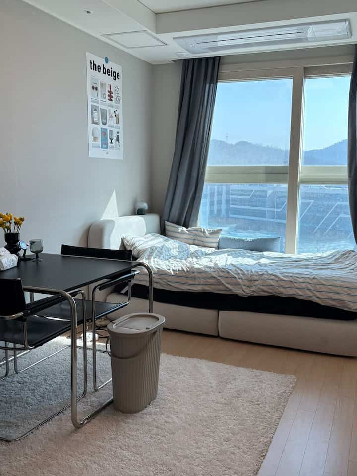 ナチュラルでホワイトトーンの6坪ワンルーム、大きな窓とベッド、ダイニングテーブルが効率的に配置された清潔な一人暮らしの空間