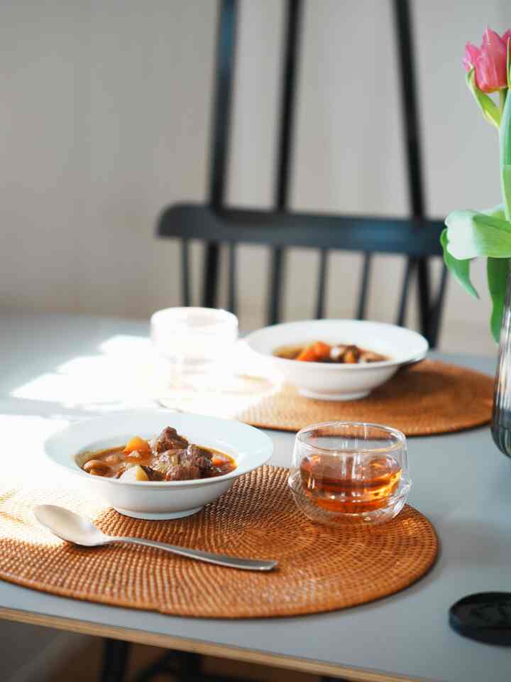 白と茶色の色調のダイニング、無印良品のテーブルマットとKINTOのグラスが配置された雰囲気のあるおうちカフェ空間