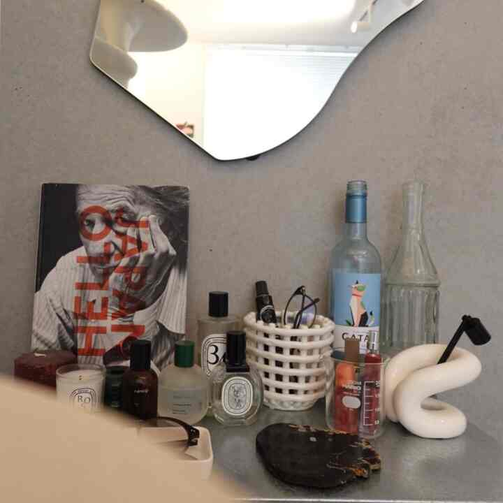 落ち着いたグレーの背景、一人暮らしの空間で整頓された香水や小物が置かれた棚とデスクのある雰囲気あるインテリア