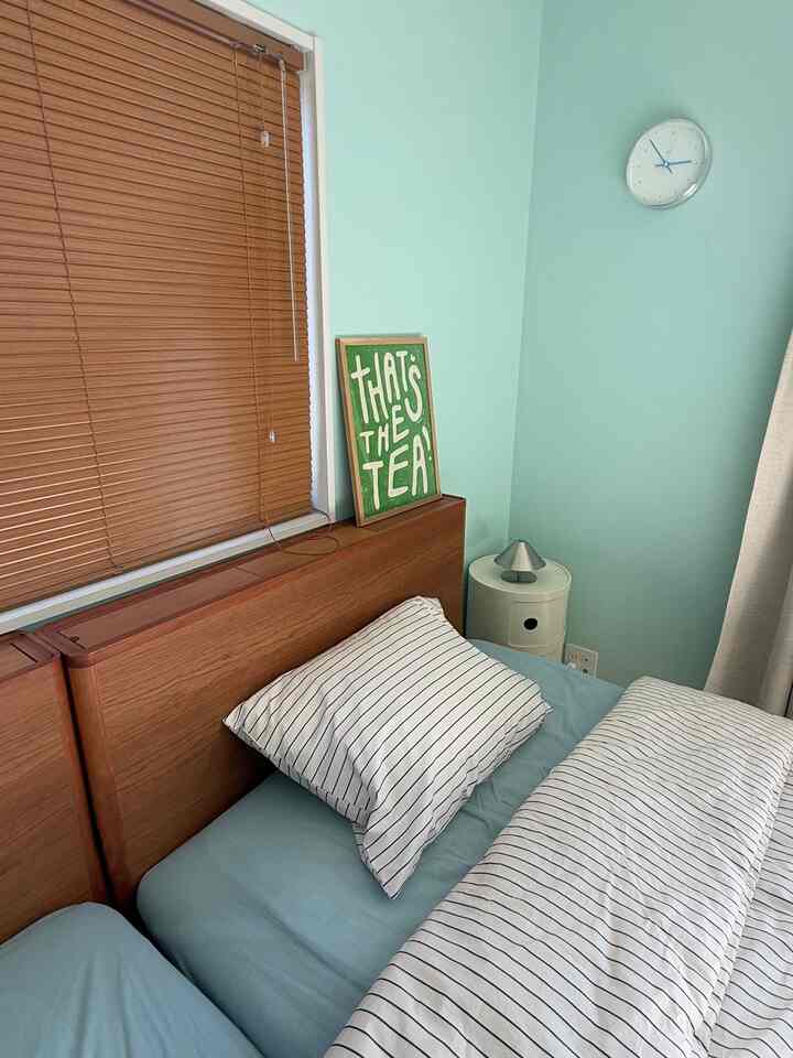 ミント色の壁とブラウンのブラインド、ボーダー柄の布団と枕が配置されたシンプルな寝室の雰囲気あるインテリア