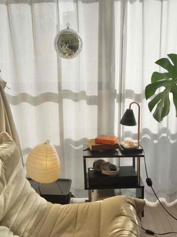 A cozy small living room with natural tones featuring a cream sofa, AKARI floor lamp, and black side table amid soft filtered light