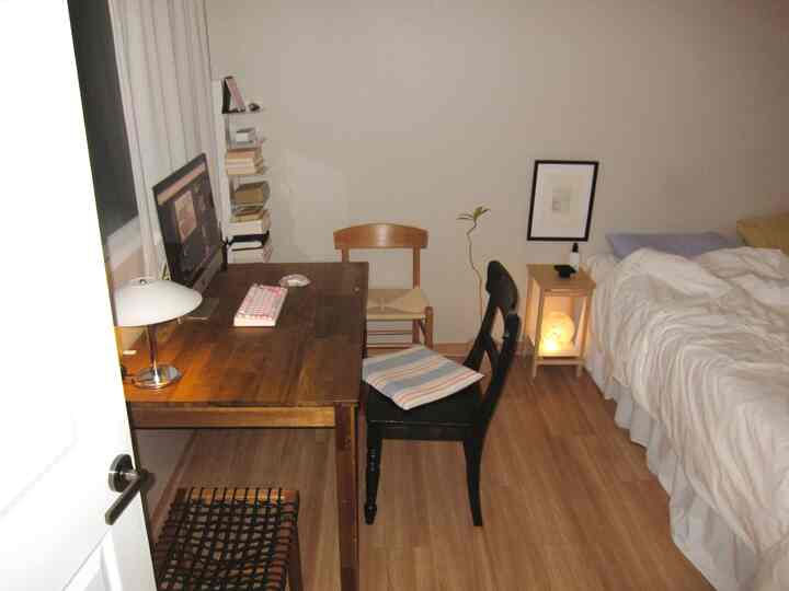 白い壁と木製家具が調和した居心地の良い一人暮らしの部屋、デスクとベッドが整然と配置されたホームオフィス兼寝室空間