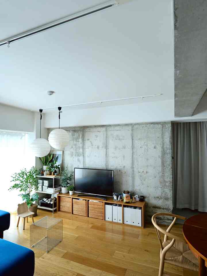 ナチュラルトーンの木製フローリングとコンクリート壁が調和したリビング、ペンダントライトと多くの観葉植物が配置された雰囲気のあるインテリア