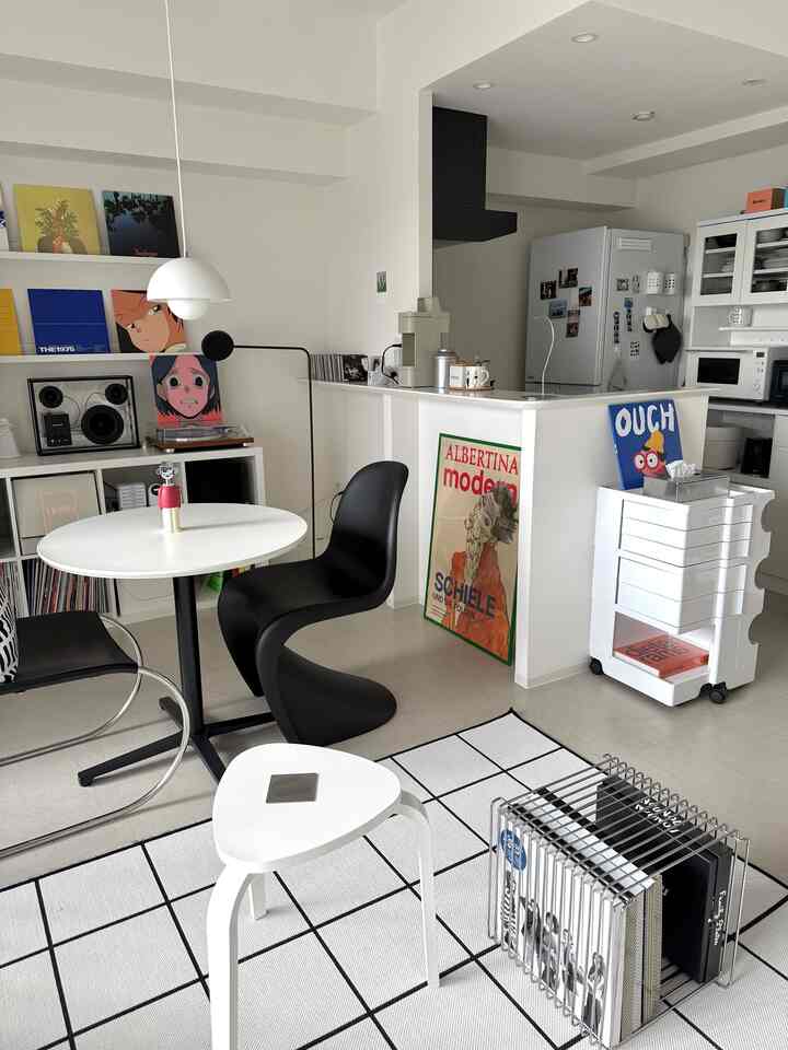 Modern living room with white and black tones, featuring a round table, Panton chair, and retro vinyl records for a stylish atmosphere