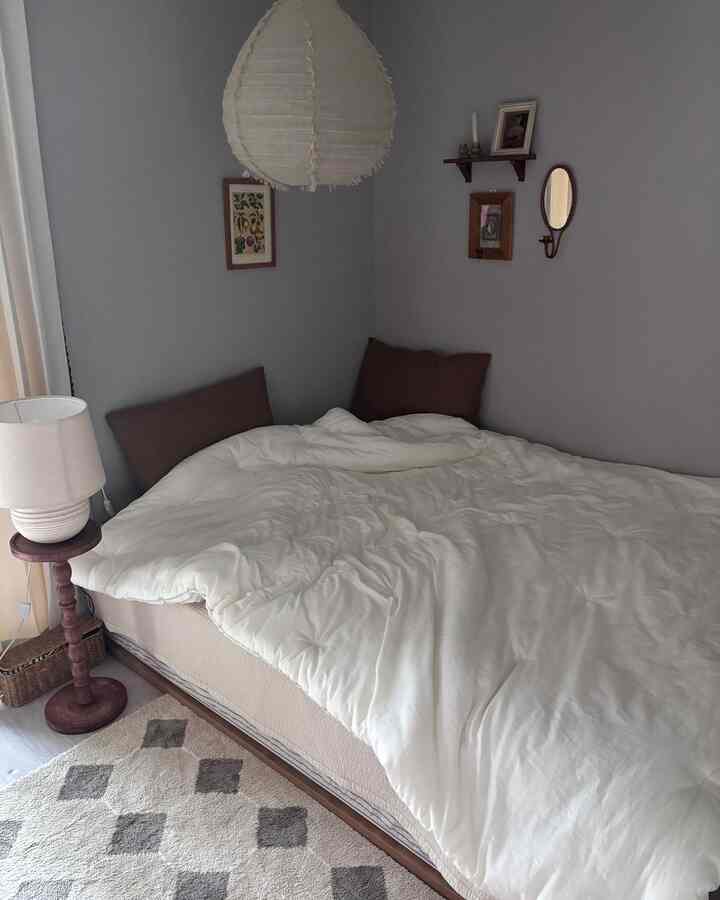 ナチュラルカラーとモダンスタイルの寝室、白い寝具と木製ベッドフレーム、テーブルランプとラグが温かみのある印象的な空間