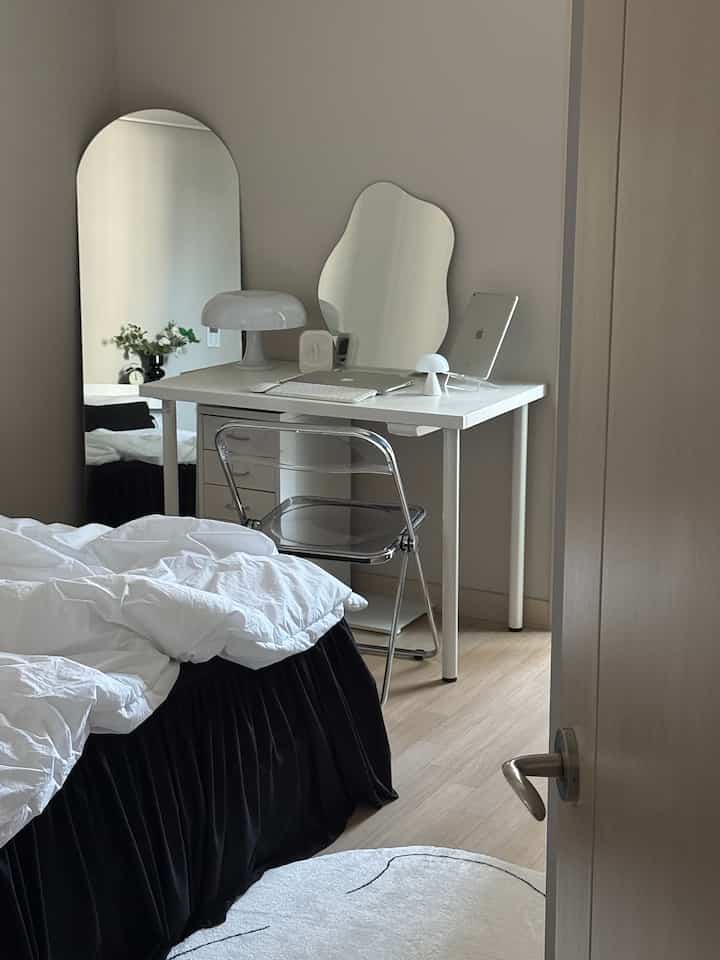A modern and cozy bedroom in white and black tones, featuring a transparent chair and simple desk setup