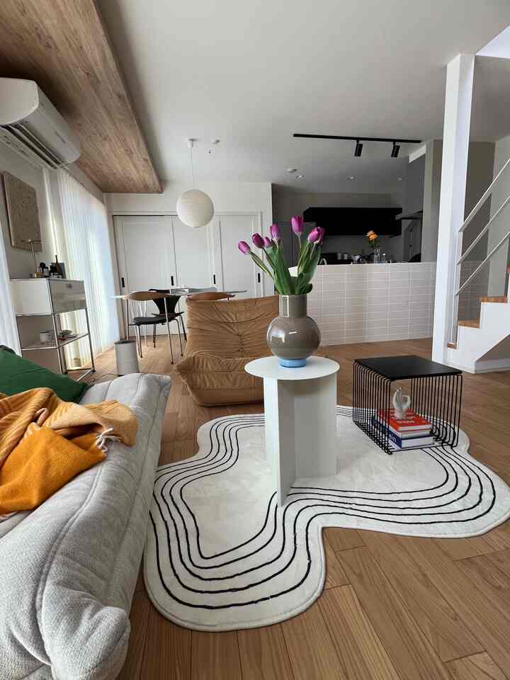 ナチュラルな色調のリビング、木製フローリングとグレーのソファ、ブラウンのアームチェア、白いラグとペンダントライトが配置された雰囲気のあるインテリア