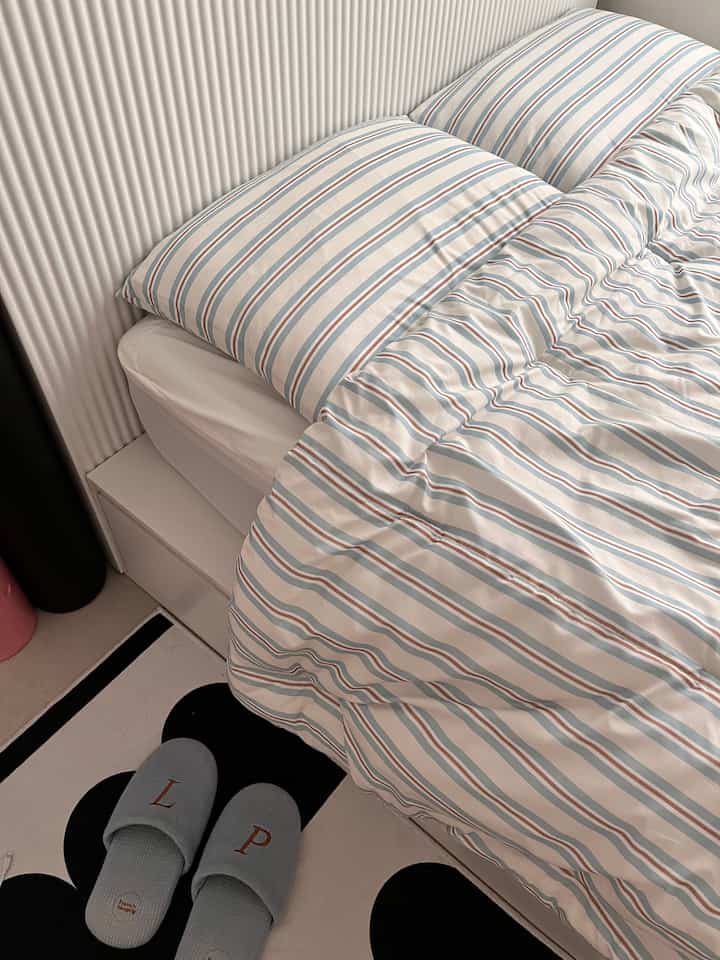 Cozy newlywed bedroom with striped bedspread and white panel wall, featuring rug and slippers on floor