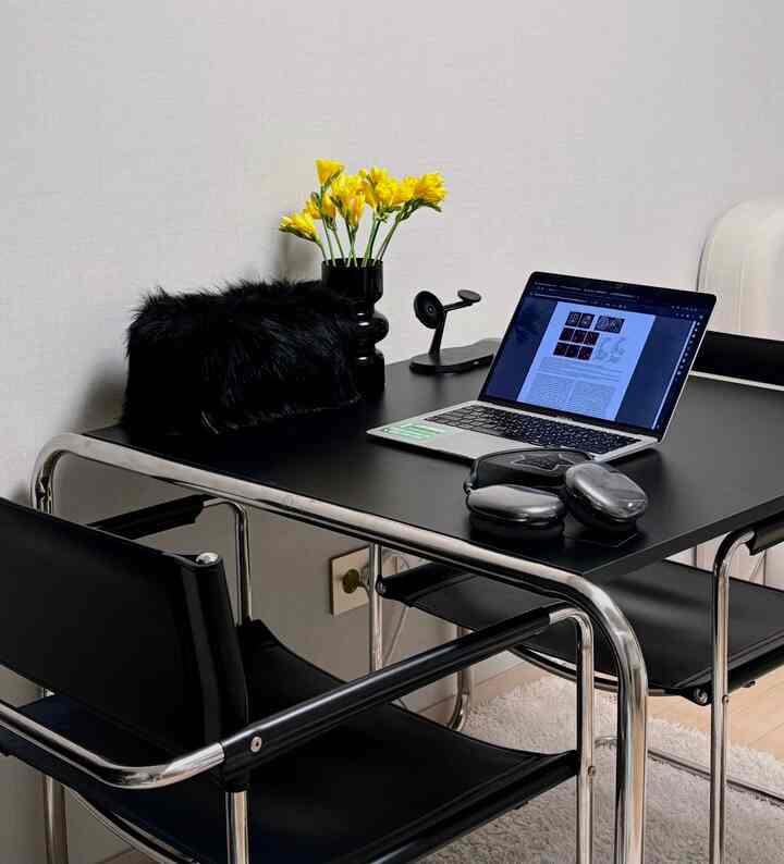 A black-dominant dining space in a 6-pyeong officetel featuring yellow flowers and a laptop, creating a cozy home cafe atmosphere