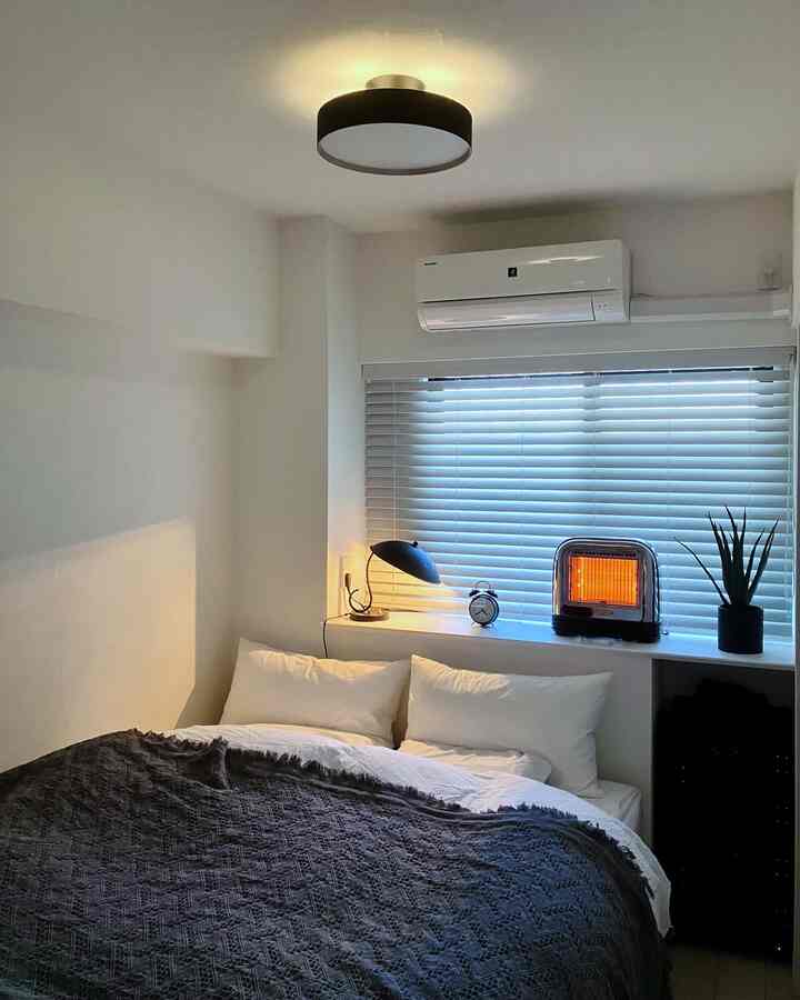 白とグレーのトーンの寝室、窓辺に置かれたブラインドとヒーターが配置された雰囲気のあるインテリア