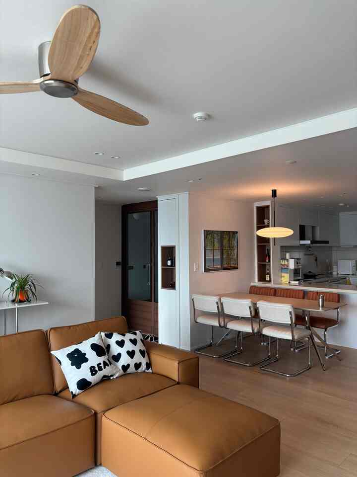 Modern living and dining room with wood tones and white hues, featuring a tan leather sofa and dining chairs