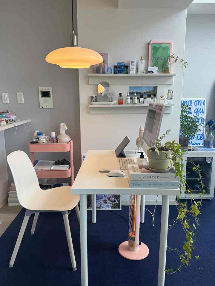 ホワイトとブルーのトーンが映えるワンルームのホームオフィス、シンプルなデスクとオフィスチェア、ペンダントライトと棚、植物が配置された落ち着いた雰囲気のインテリア