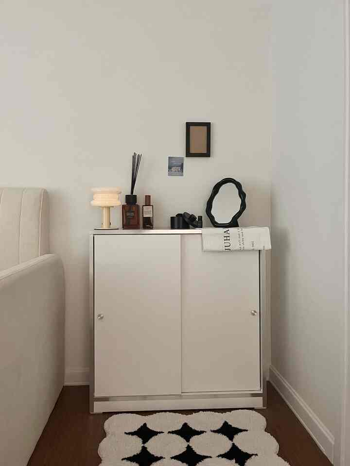 Minimal modern bedroom featuring white cabinet topped with a black irregular wave table mirror and lamp