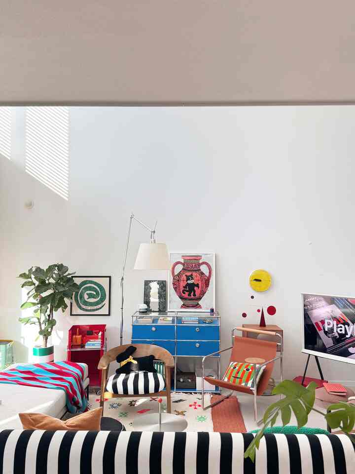 明るい白色調のリビング、ブルーのチェストと黒い犬のぬいぐるみが置かれたストライプのアームチェアが配置された印象的な空間