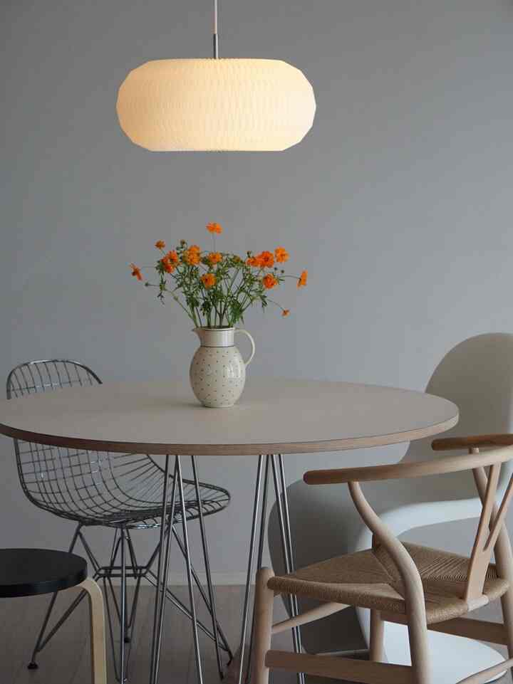 グレーの壁とナチュラルウッドの椅子があるシンプルなダイニング、中央に丸いダイニングテーブルとペンダントライトが配置された空間