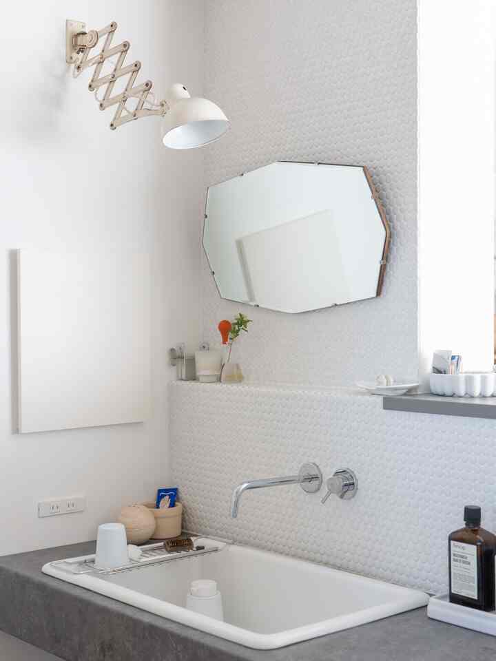 白を基調としたバスルームに設置された洗面台と鏡がある、ミニマルで雰囲気のあるインテリア