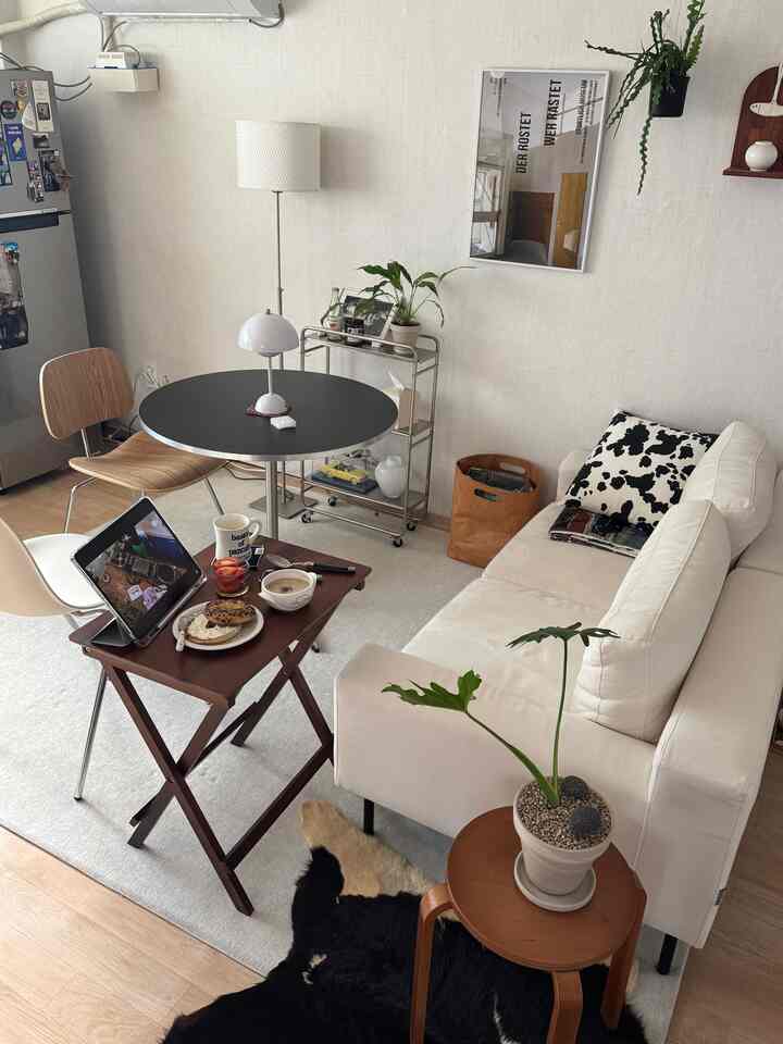 Compact living room in white and black tones featuring sofa, round dining table, plants, and cozy ambient lighting