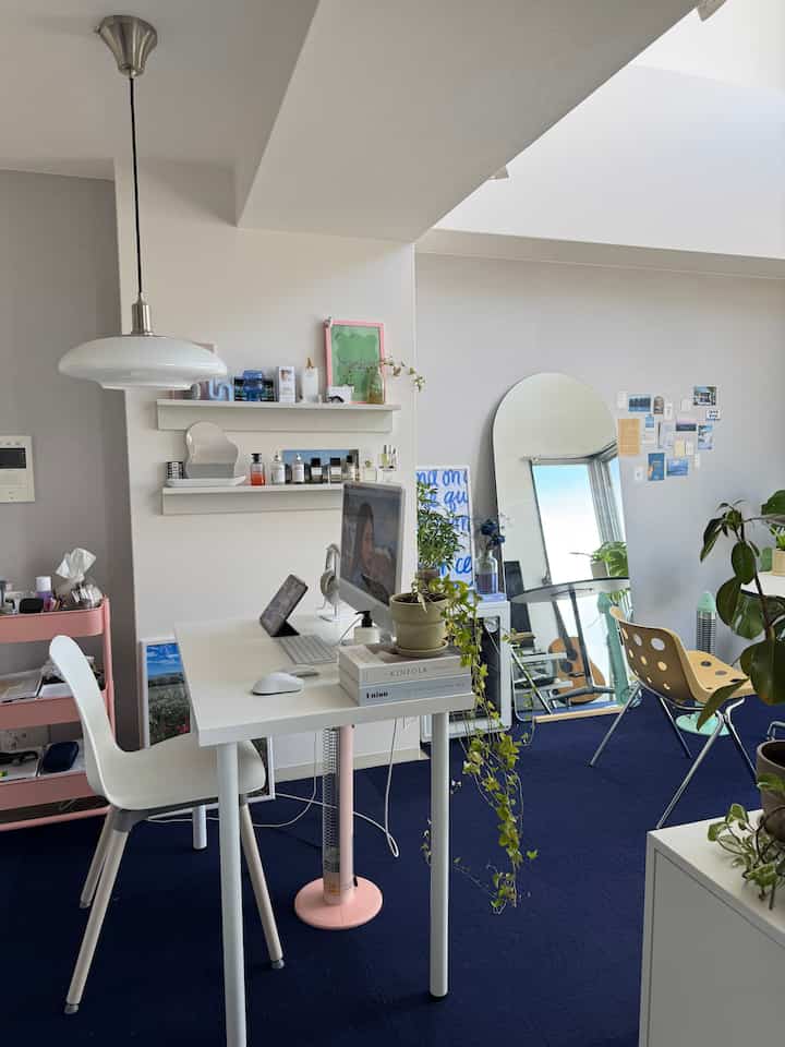 Minimalistic studio apartment home office in white and navy blue tones, featuring mid-century modern desk and chairs, plants, and large arched mirror