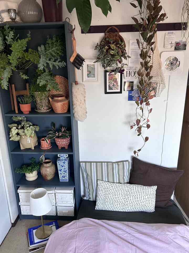 ナチュラルな色合いの寝室、青い本棚に植物や小物が飾られたシンプルな印象の空間