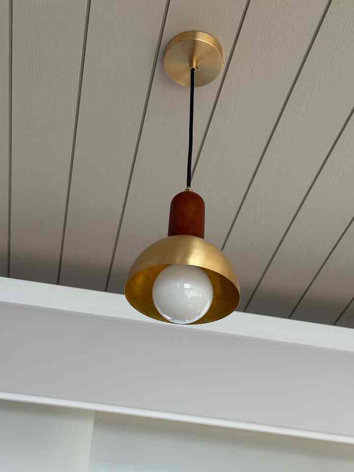 Gold and wood tone pendant light hanging from a simple ceiling interior