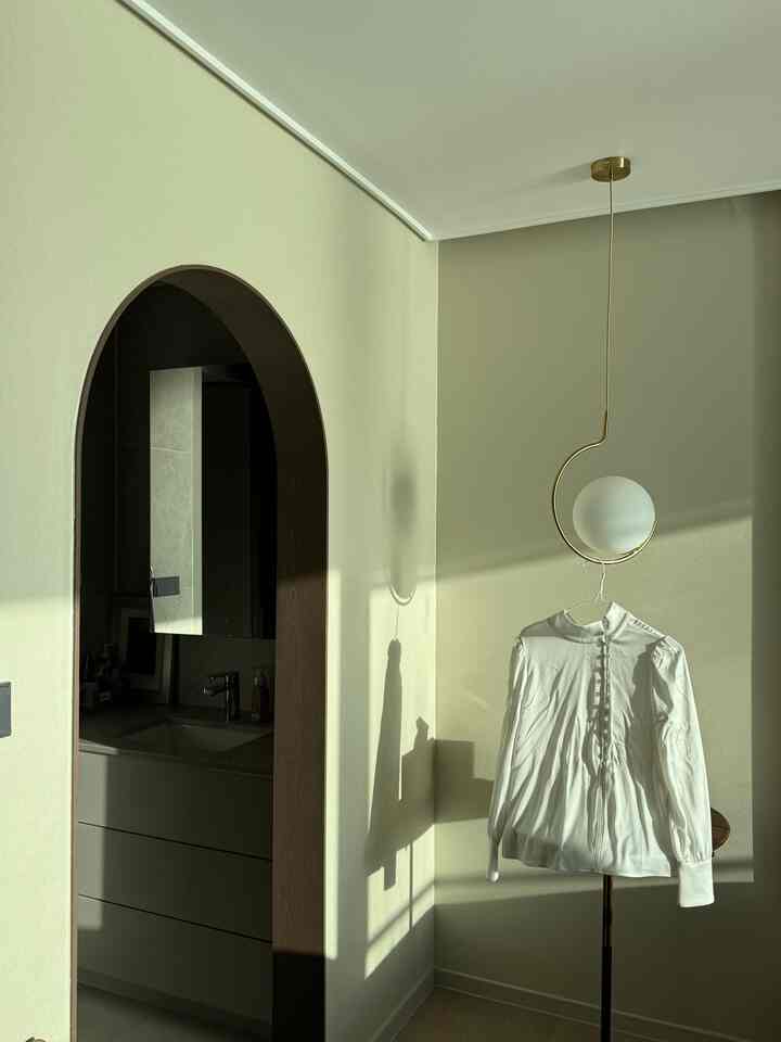Beige-toned closet space with wooden arch, featuring a white blouse and glass pendant light creating a cozy atmosphere