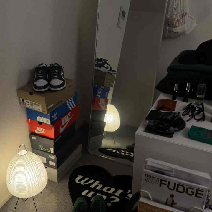 白と黒のトーンの玄関スペース、全身鏡と整然と積み重ねられた靴箱が配置された実用的な空間