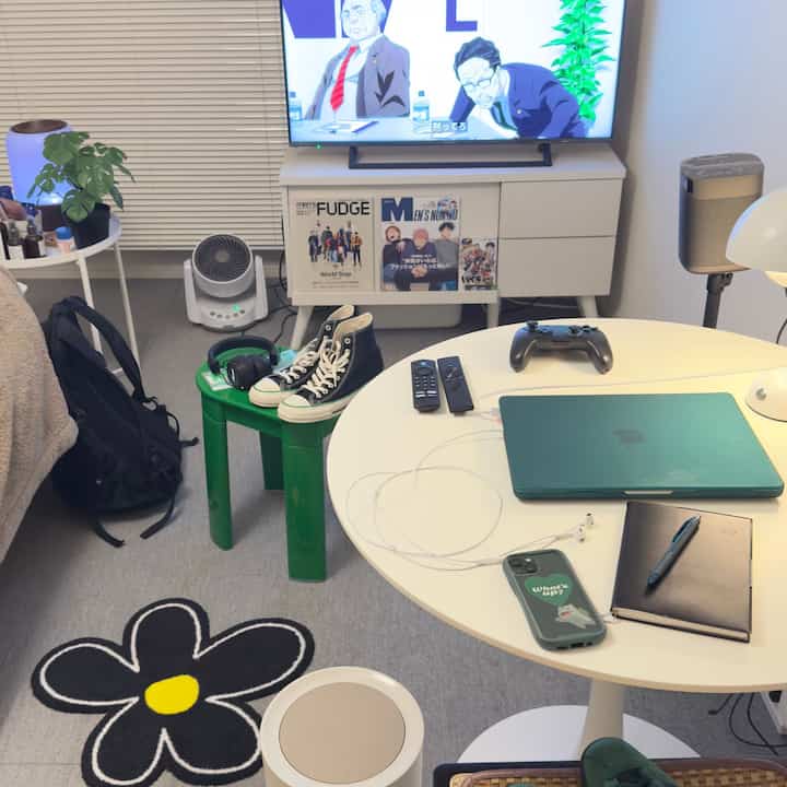 白を基調とした一人暮らしの小さな部屋、円形テーブルにノートパソコンやリモコン、ゲームコントローラーが置かれたモダンな空間