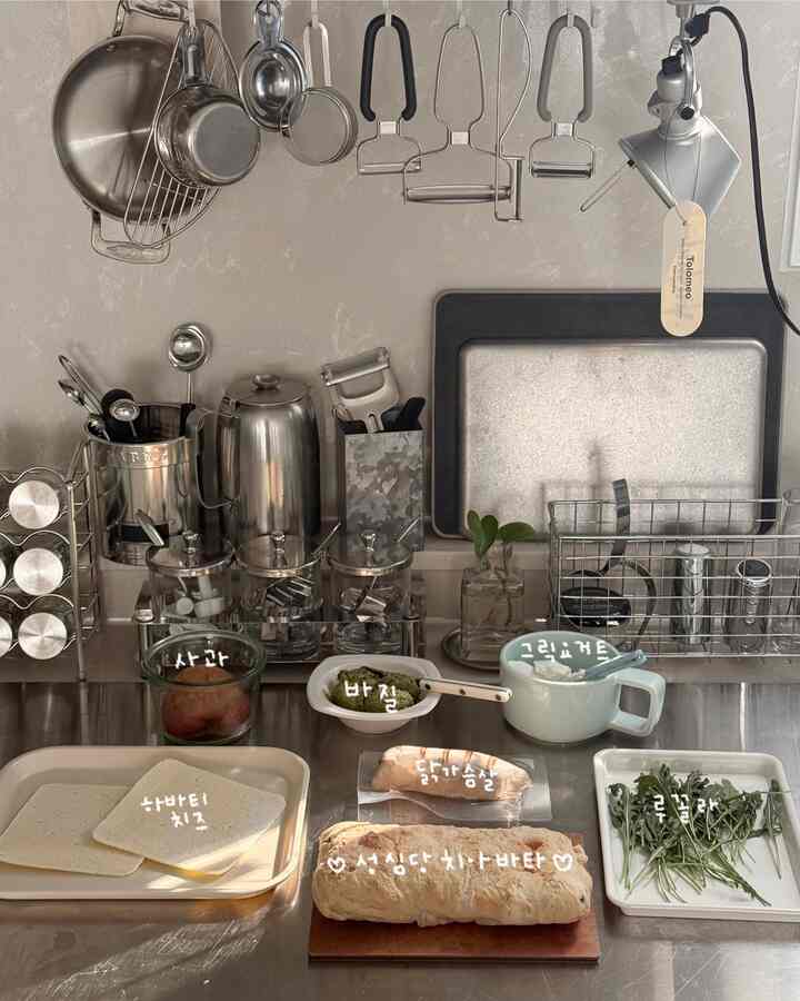 落ち着いた白とグレーの色調のキッチン、ステンレス製の調理器具と新鮮な食材が整然と配置された雰囲気のあるインテリア