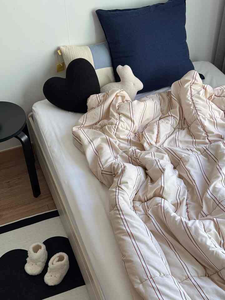 Beige and black toned bedroom featuring a bed with cushions and a stool, creating a cozy atmosphere