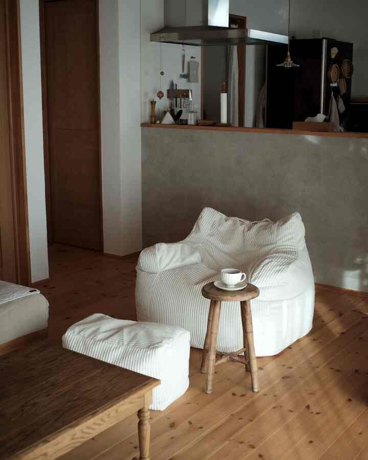Minimal living space for single household featuring natural wood tone flooring, white bean bag sofa, and wooden stool