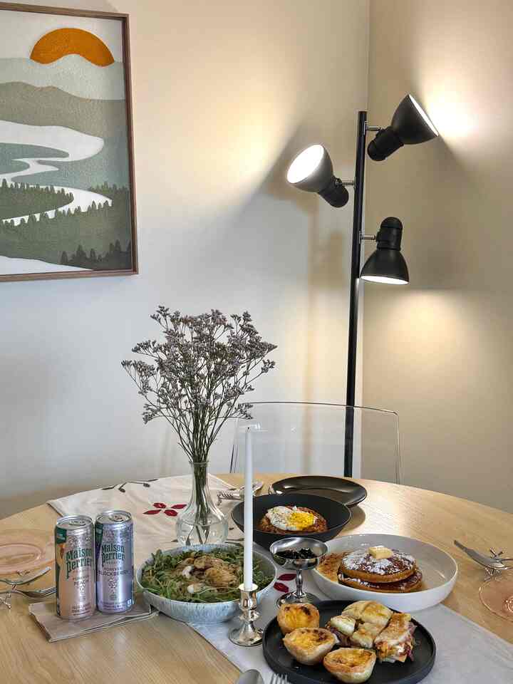 Light brown round dining table in a dining room with a table runner, vase, and assorted plates of food creating a cozy atmosphere